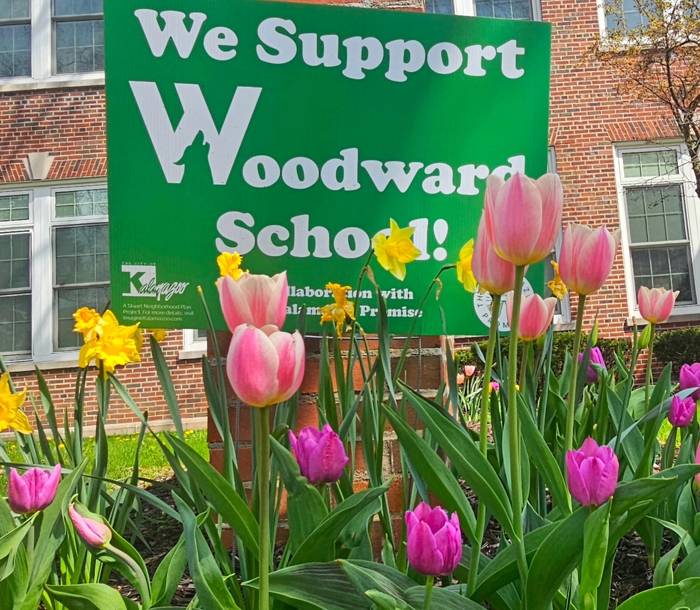 Spring flowers with "We Support Woodward School" sign